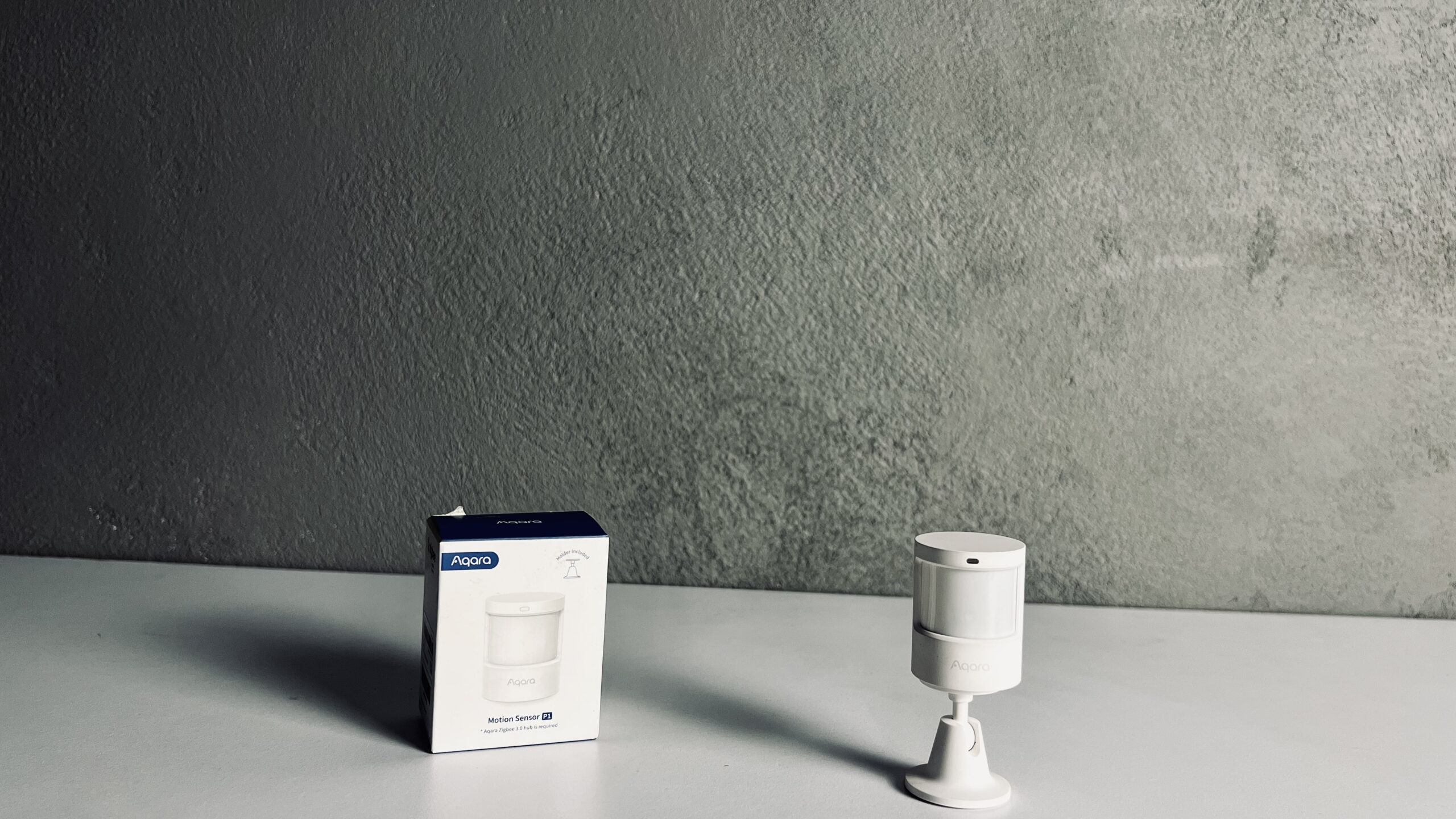 Aqara P1 motion sensor with packaging on white surface against gray background