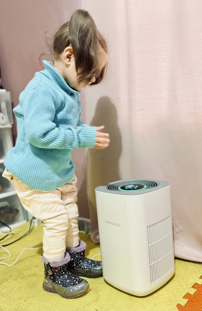 A toddler wearing a blue sweater standing on a yellow surface trying to turn on the Purel through its touch display