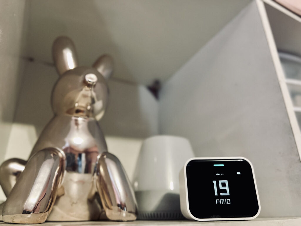 Air Monitor Lite displaying PM10 levels on white shelf next to a silver bunny figurine