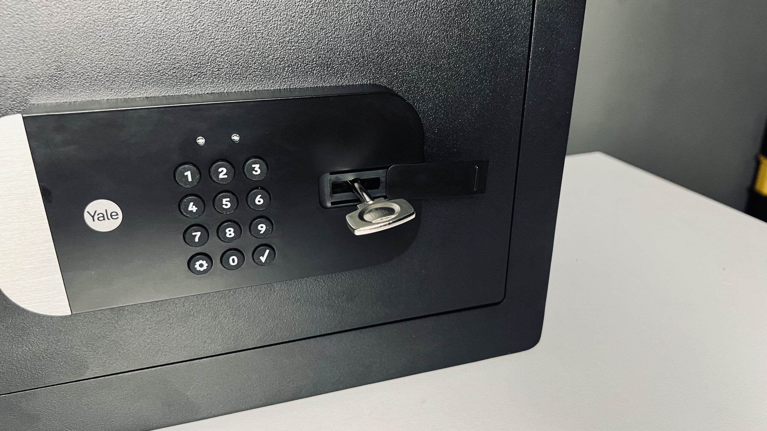 a black safe with an electronic keypad angled on a white surface against a gray walls with black acoustic panels