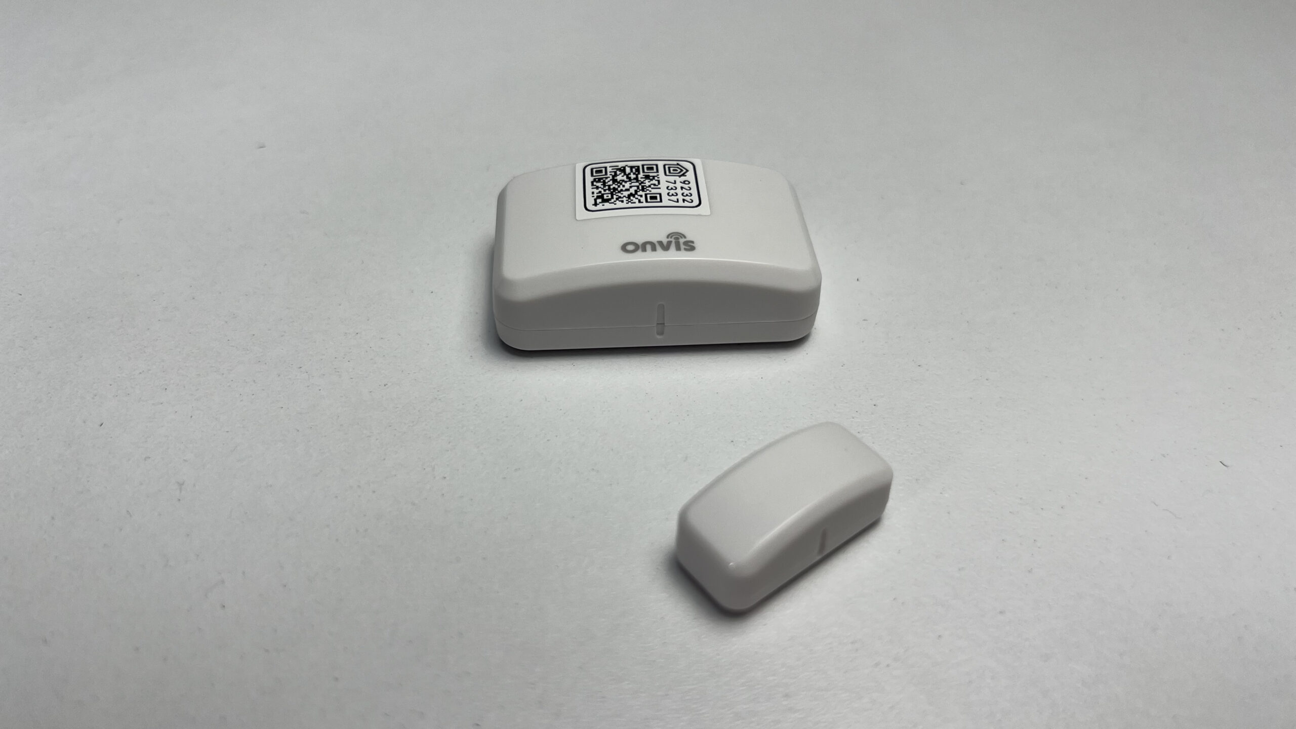 a small, white, rectangular device with a detached smaller white piece on a white surface against a gray background, the Onvis CT3 Door & Window Contact Sensor