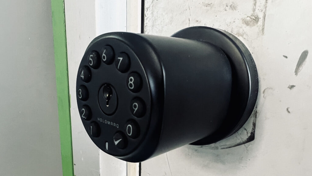 an installed matte black door knob with a horseshoe-shaped keypad on the outer edge of the face of the knob, the Holomarq Sequra Smart Door Knob