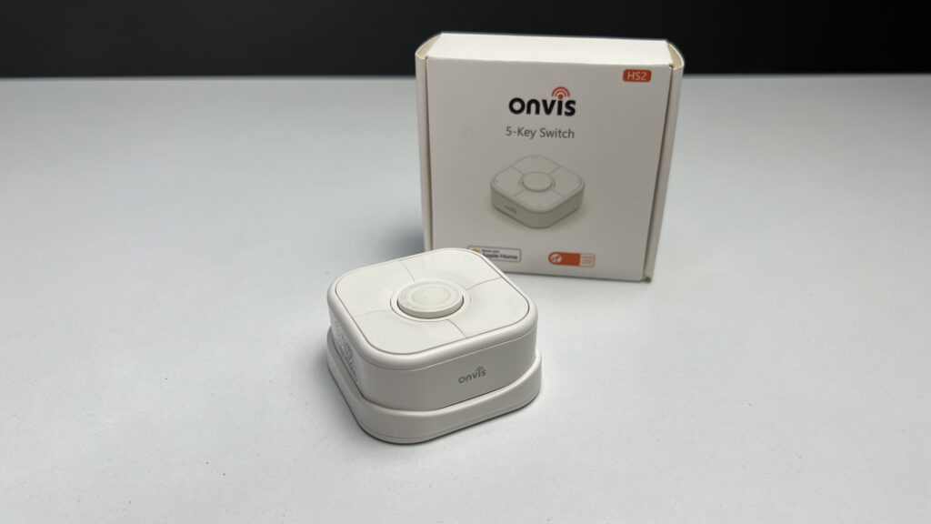 The Onvis HS2 Smart Button alongside its packaging on a white surface against a gray wall