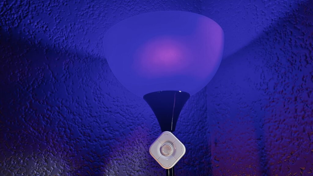 The HS2 magnetically mounted on a standing lamp illuminated in blue in the corner of a gray-walled room